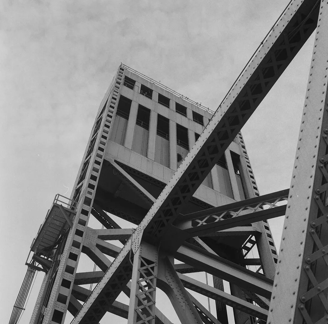 Black and white photo of the structural details of a steel bridge with riveted girders and a large vertical tower.